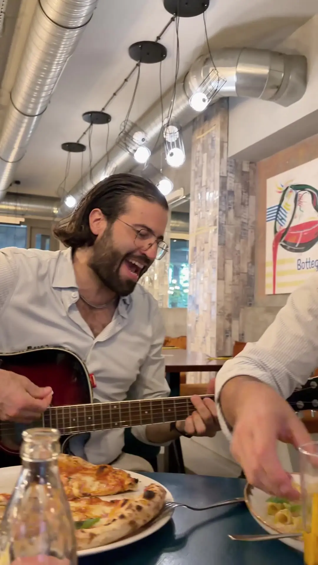 Francesco gra na gitarze przy stoliku, obok pizza — czwartek w Bottegas przy ul. Oboźnej